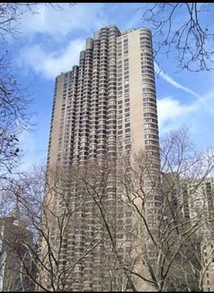 A tall building with many windows is surrounded by trees.