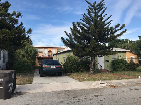 A car is parked in front of a house with a tree in front of it.