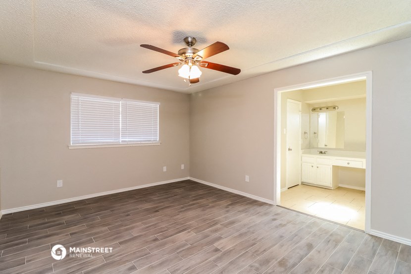 the spacious living room with wood flooring and a ceiling fan