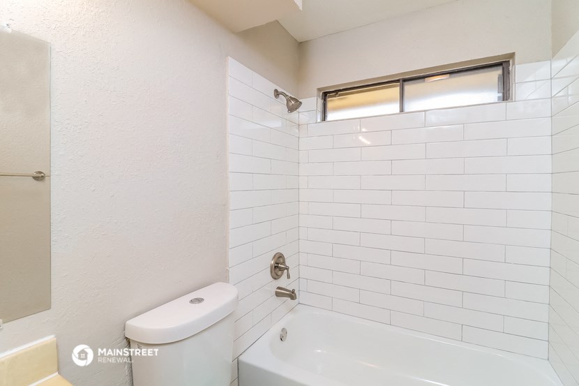 a bathroom with white tiles and a tub and a toilet