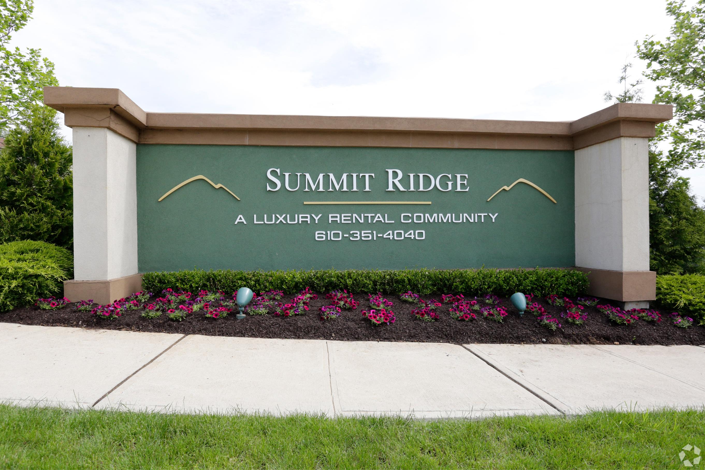 a sign for summit a luxury rental community with flowers and a sidewalk