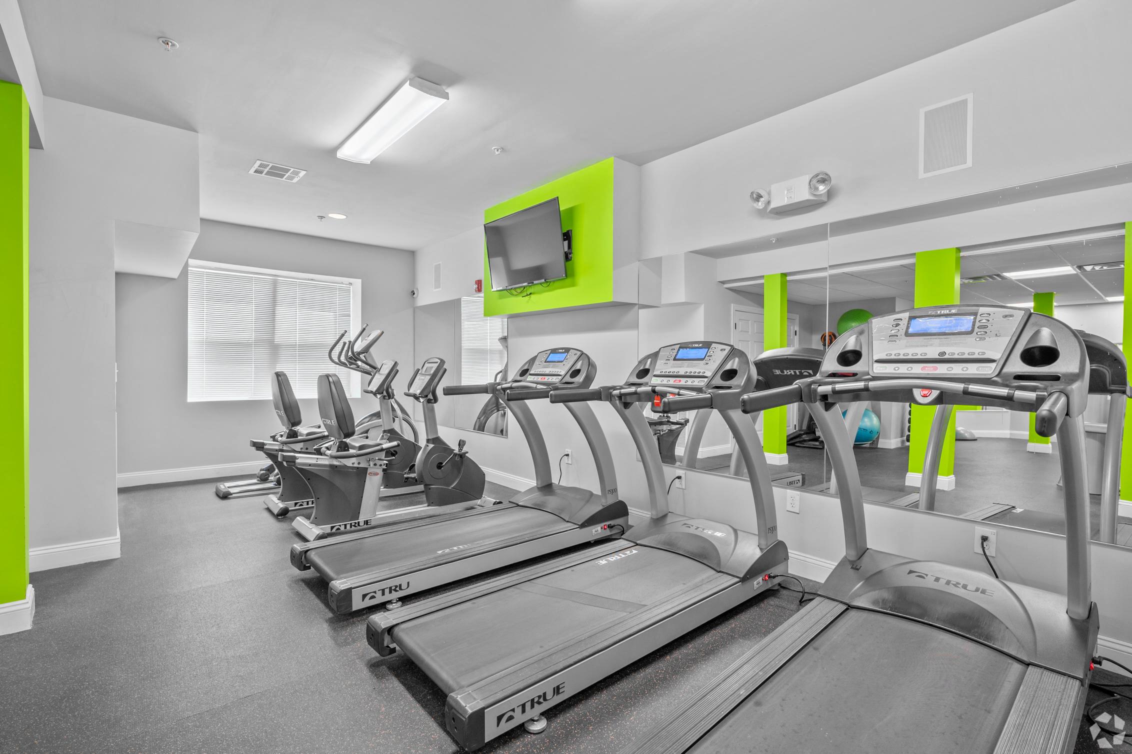 a gym with cardio equipment and a television