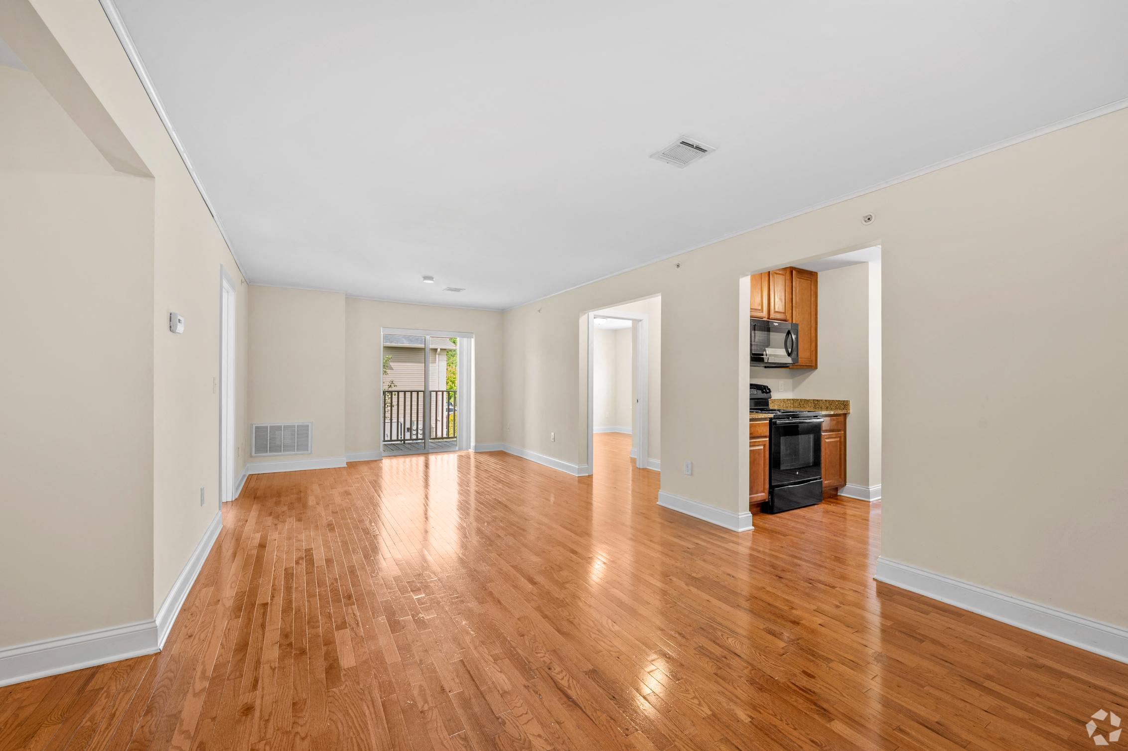 an empty living room with wood floors and a kitchen