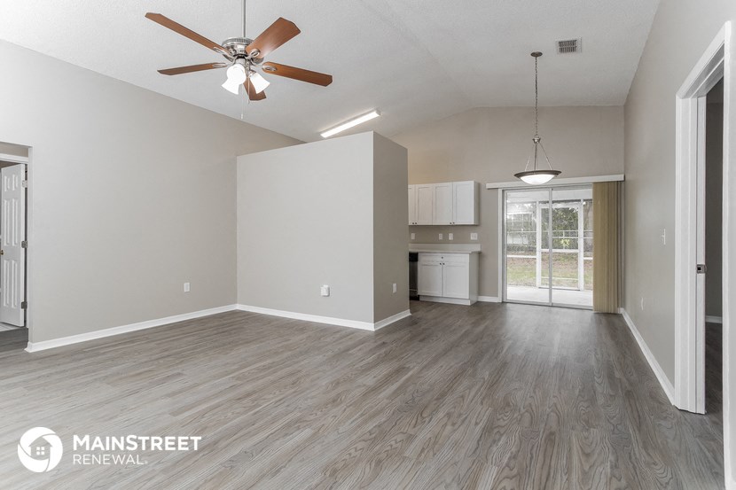 an empty living room with a ceiling fan and a kitchen