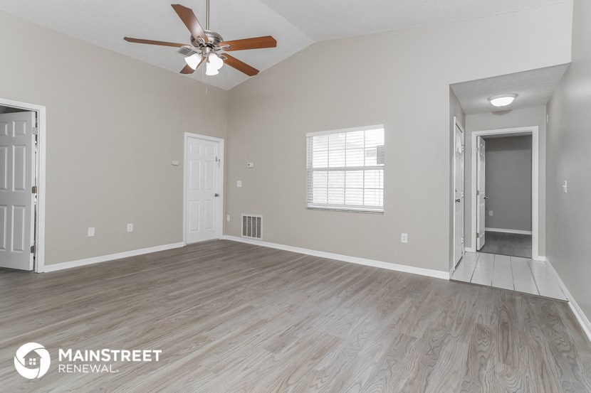 the spacious living room with a ceiling fan and wood flooring