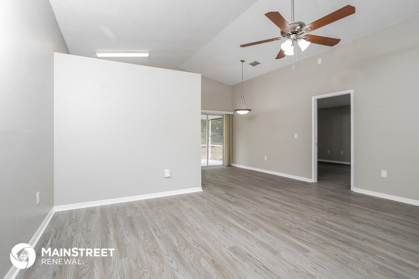 the spacious living room with a ceiling fan and white walls