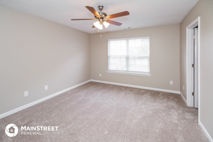 the spacious living room with carpeted floors and a ceiling fan