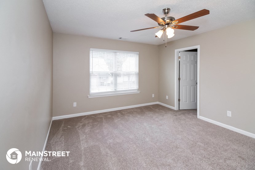 the spacious living room with carpeted flooring and a ceiling fan