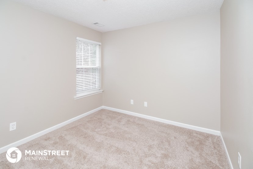 the spacious bedroom with carpeted flooring and a window