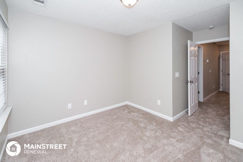 the spacious living room of an apartment with carpeting and a door to the bathroom