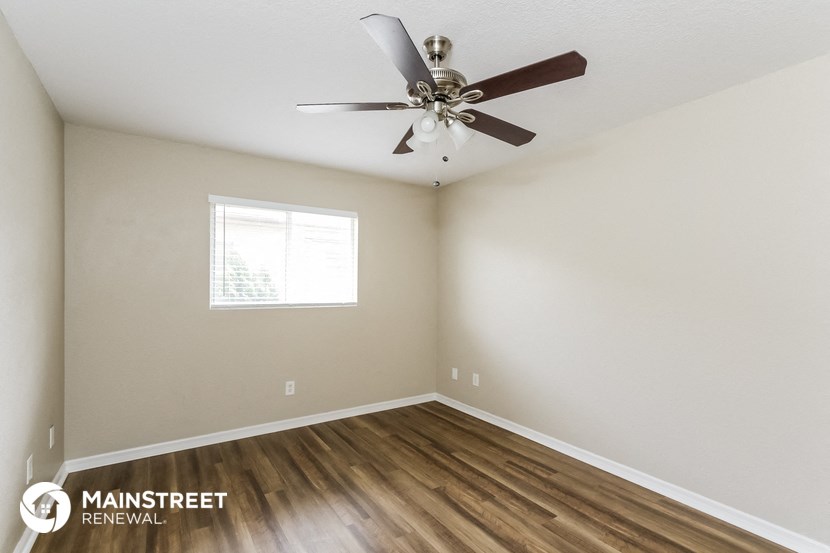 the spacious living room has a ceiling fan and hardwood floors