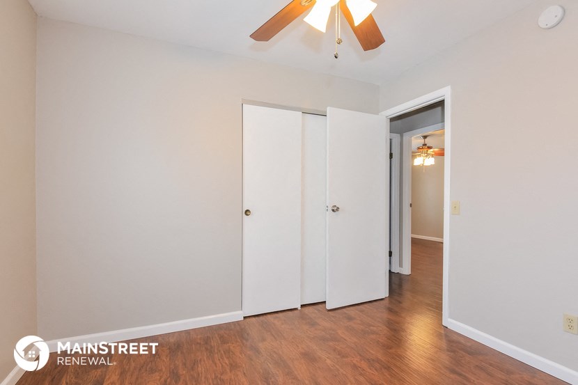 a bedroom with white walls and a wood floor and a ceiling fan