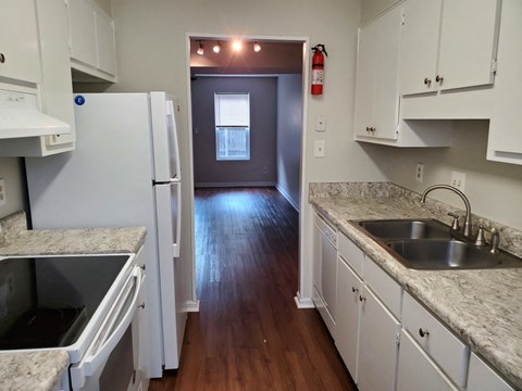 a kitchen with white cabinets and marble counter tops and a hallway with a white refrigerator