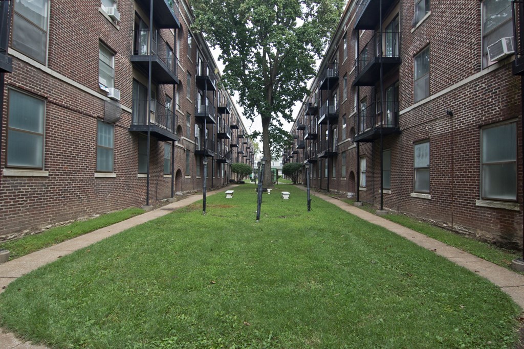 an alleyway between two brick apartment buildings with grass and trees