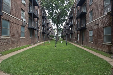 an alleyway between two brick apartment buildings with grass and trees