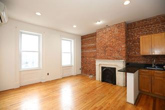 an empty living room with a brick fireplace and wooden floors