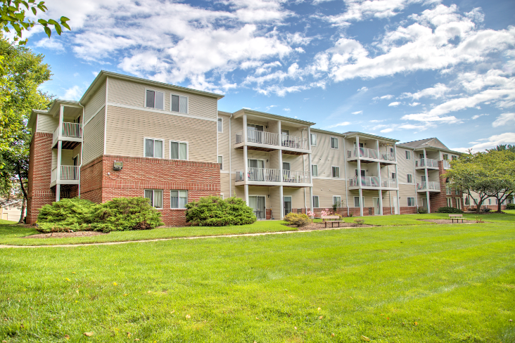 exterior of Creekside at Tasker's Chance in Frederick, MD with grass on either side of walkway to building and shrubs around building exterior
