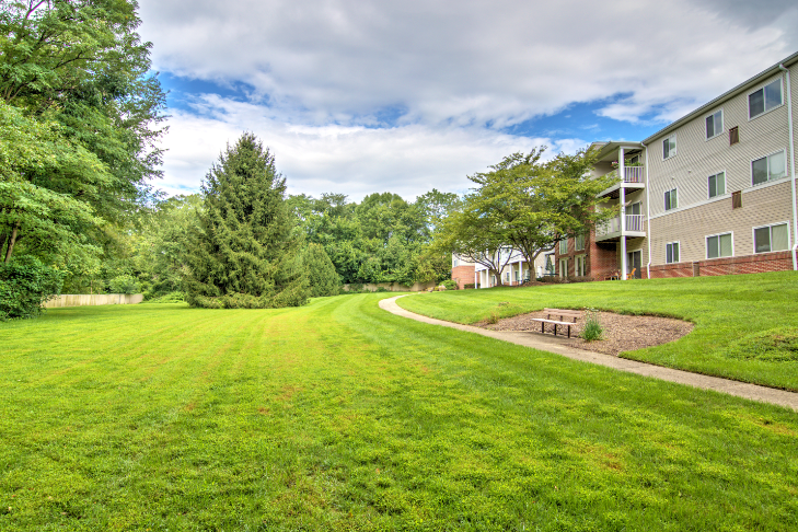 exterior of Creekside at Tasker's Chance in Frederick, MD with grass on either side of walkway and trees in back