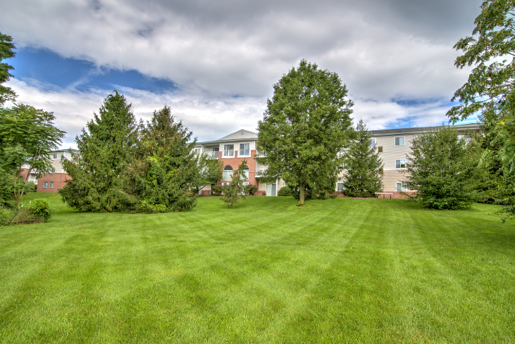 exterior of Creekside at Taskers Chance with grass, trees in back near building and blue sky with clouds