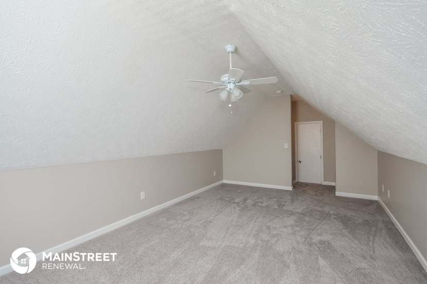 the living room of an attic with carpet and a ceiling fan
