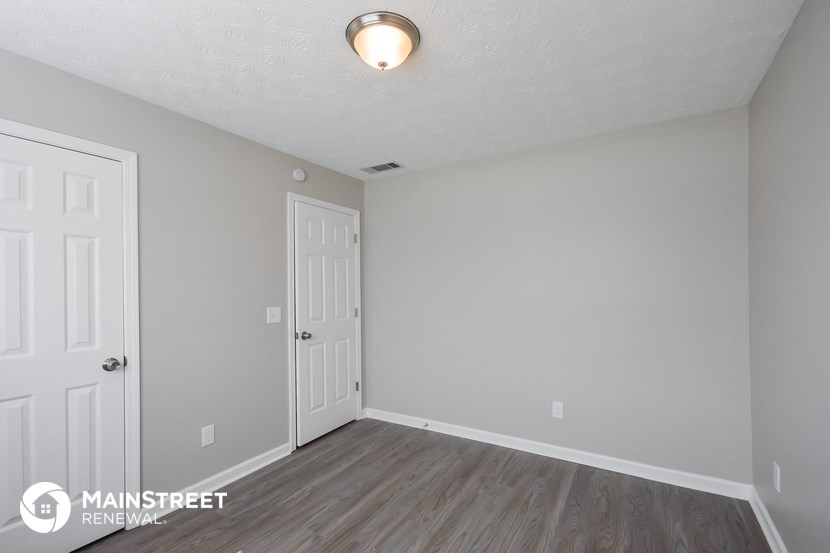 the spacious living room with white walls and wood flooring