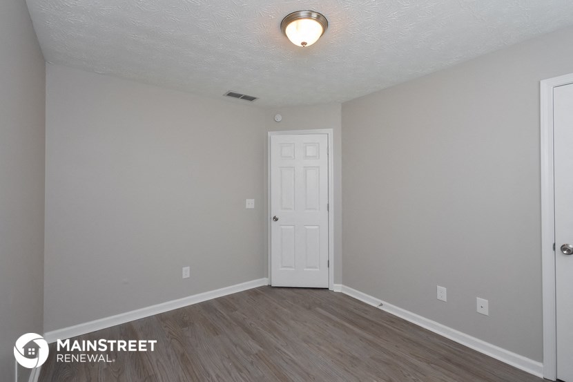the spacious living room with white door and wood flooring