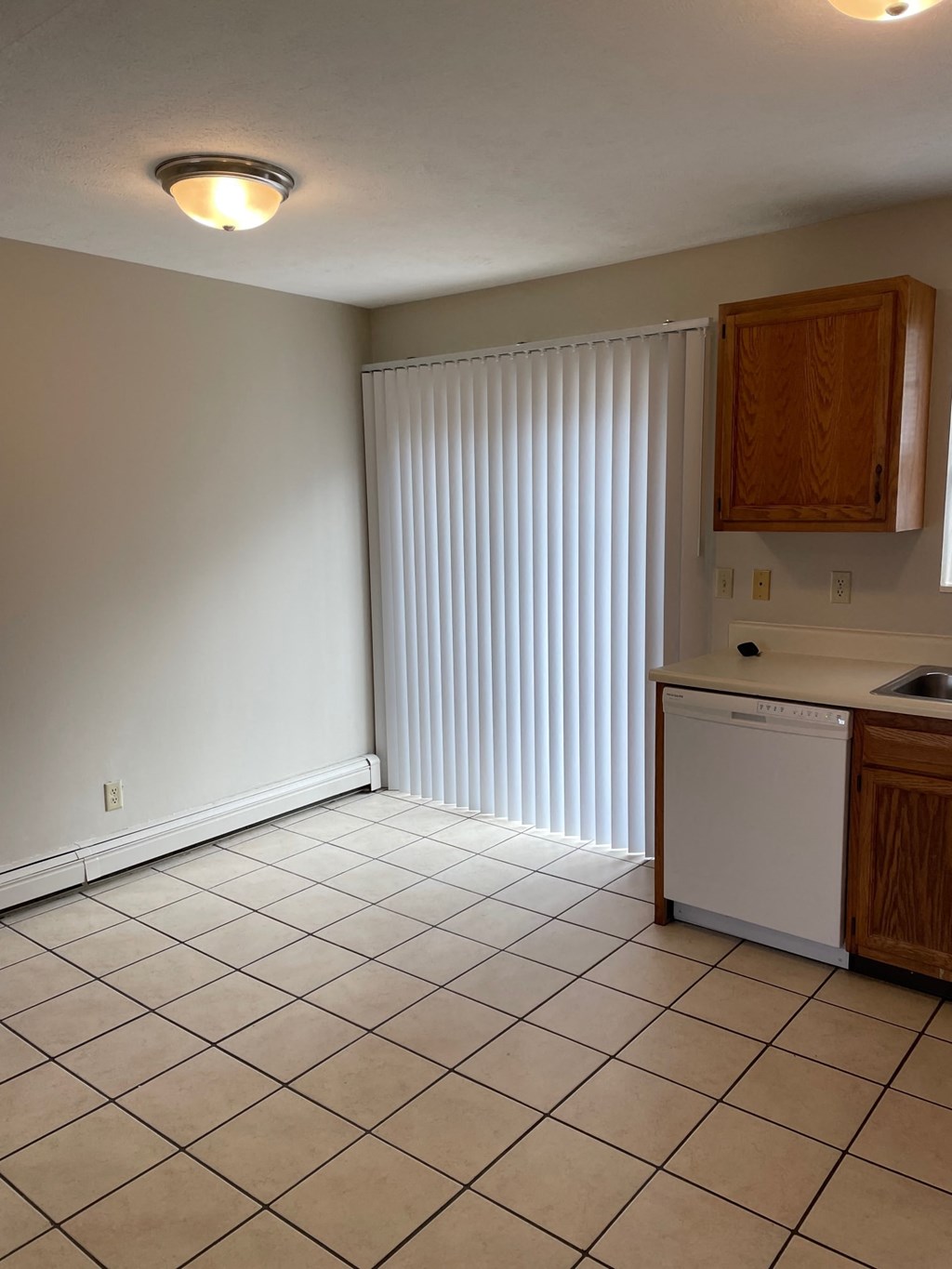 an empty kitchen with a white tiled floor and a window with blinds