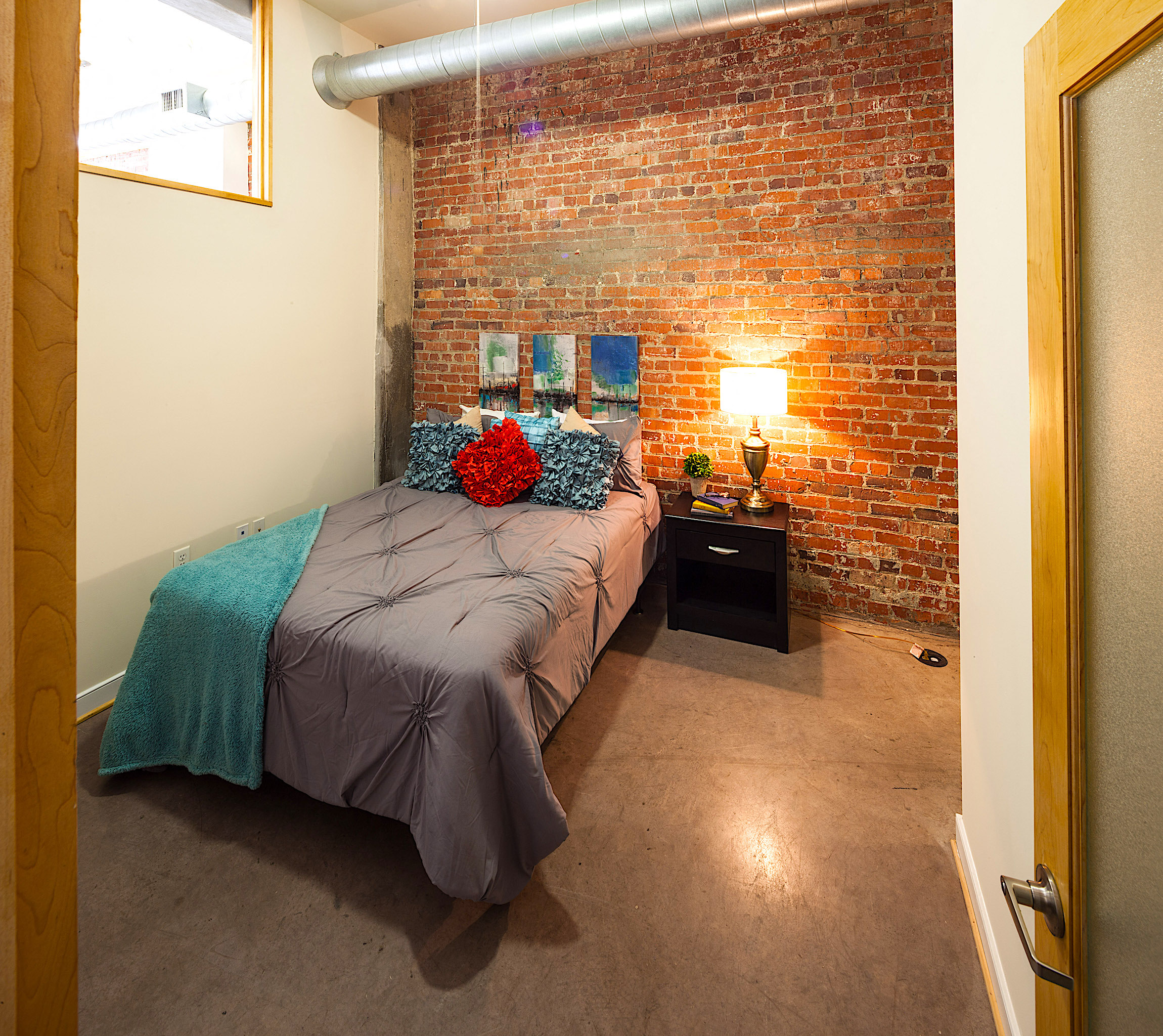 A bedroom with a brick wall and a bed with a teal blanket.