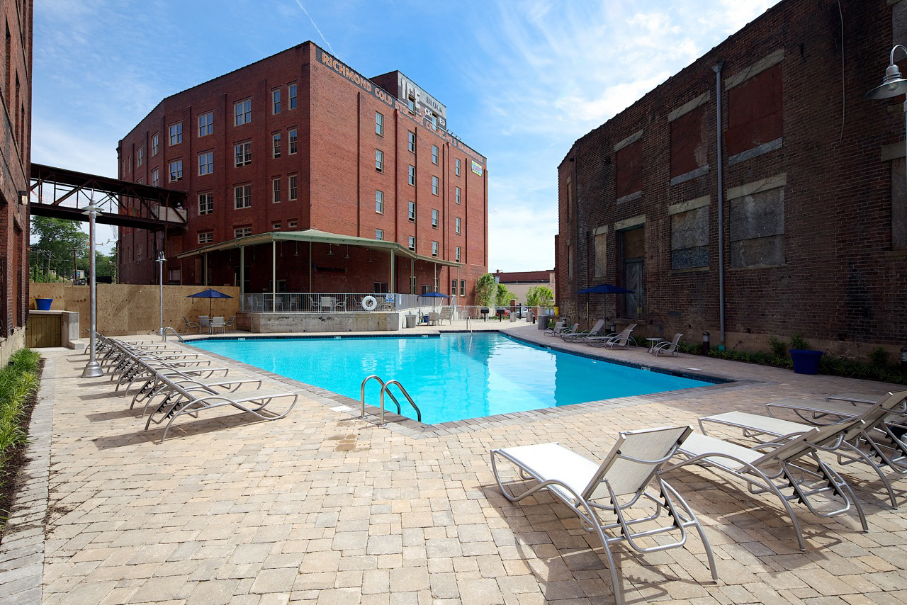 A pool surrounded by chairs in front of a brick building.