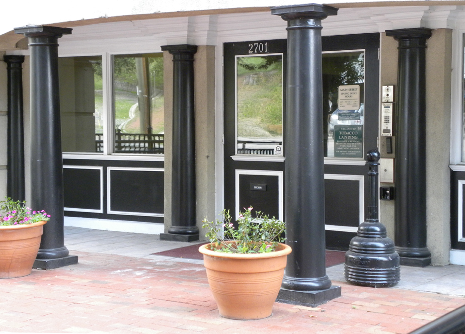 the front of a building with black pillars and potted plants