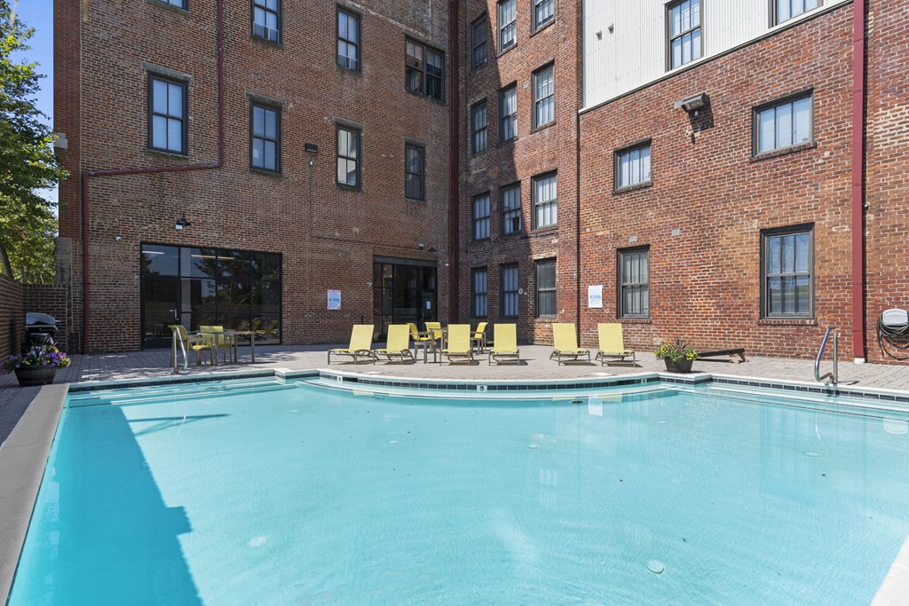 a swimming pool with yellow chairs and a brick building