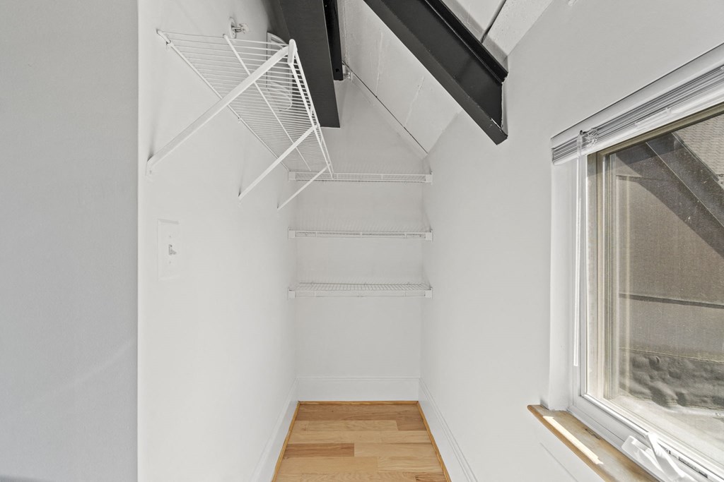 a room with white walls and a window and a white closet with shelves and hooks