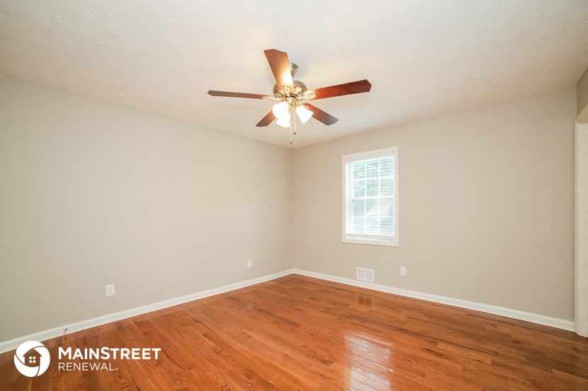 the spacious living room with wood floors and a ceiling fan