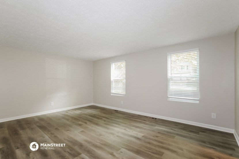 the spacious living room with wood flooring and white walls