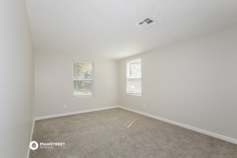 a spacious room with carpet and two windows