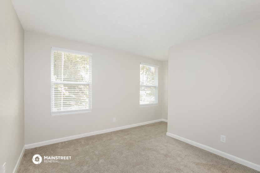 a bedroom with white walls and carpet and two windows