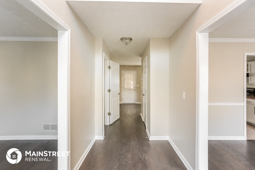 a hallway with white walls and a wood floor and a white door to a hallway
