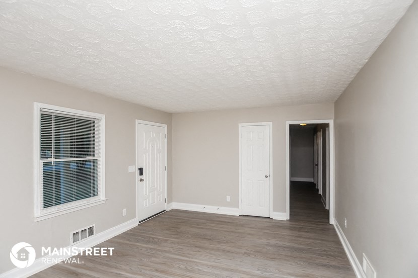 the living room of an apartment with white walls and wood flooring