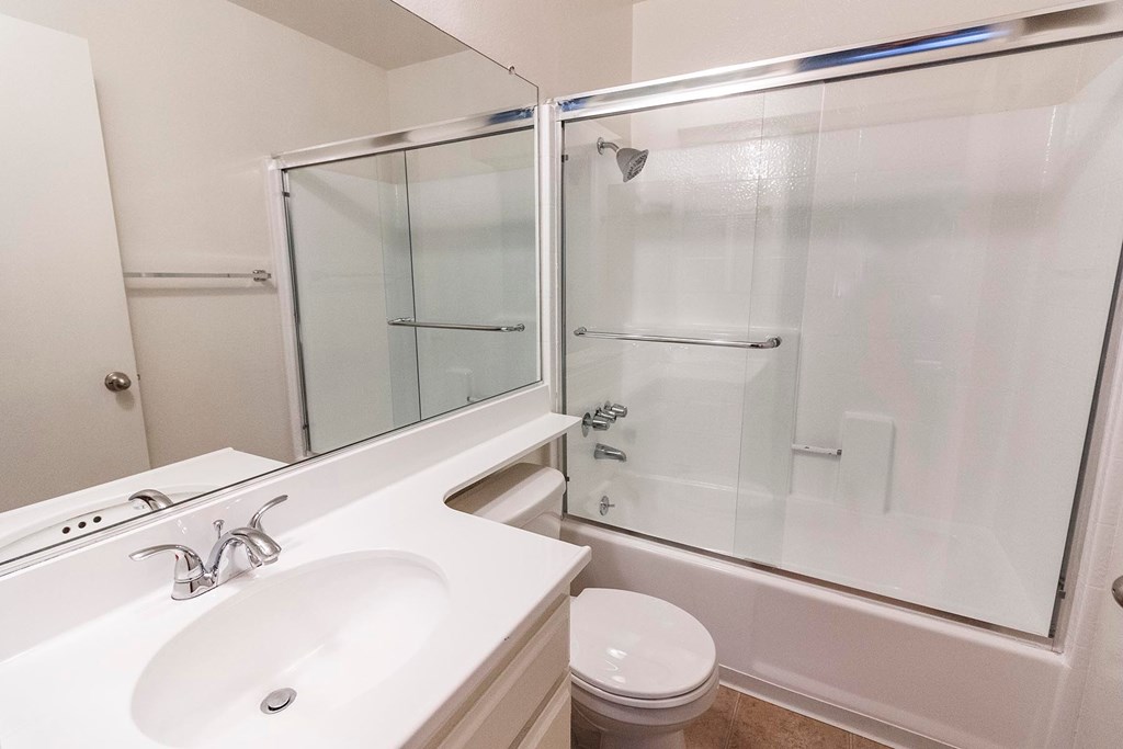A white bathroom with a sink, toilet, and shower.