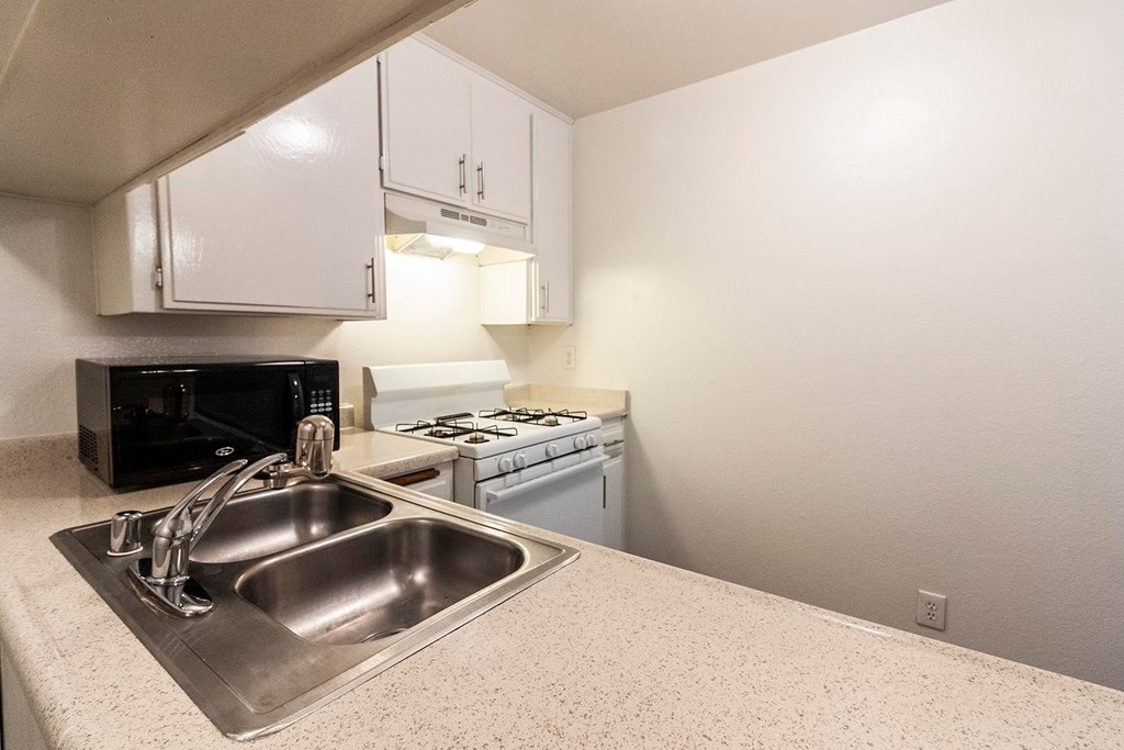 A kitchen with a stove, sink, and cabinets.