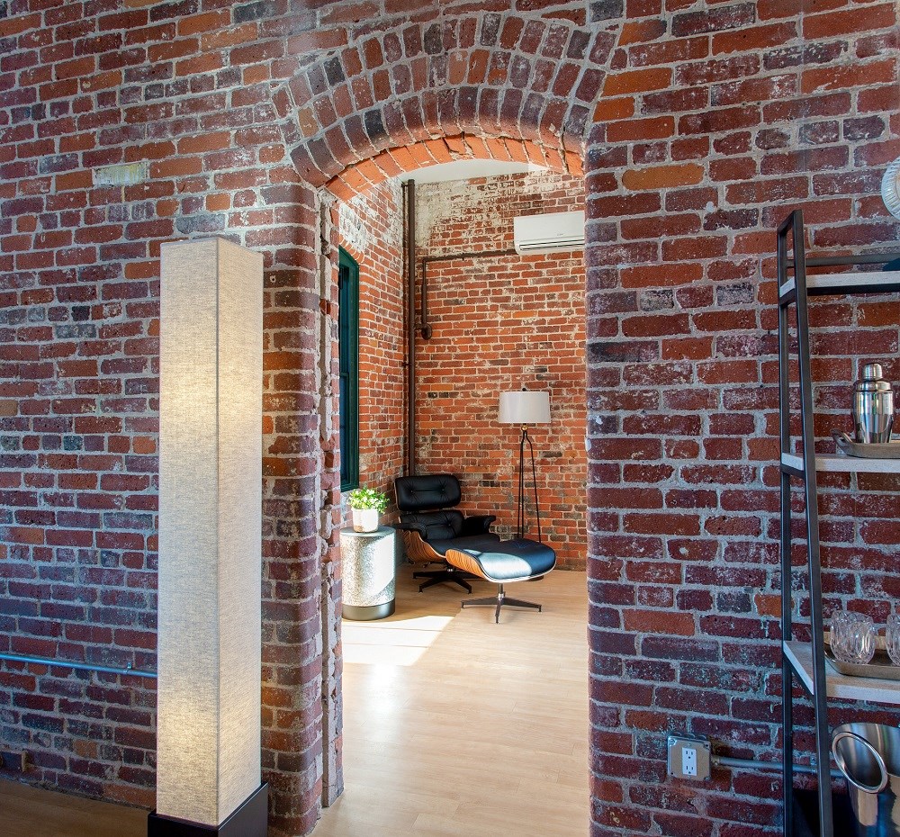 a brick archway leads into a living room with a black chair and a lamp