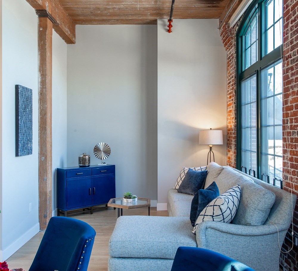 a living room with a couch and blue chairs and a brick wall