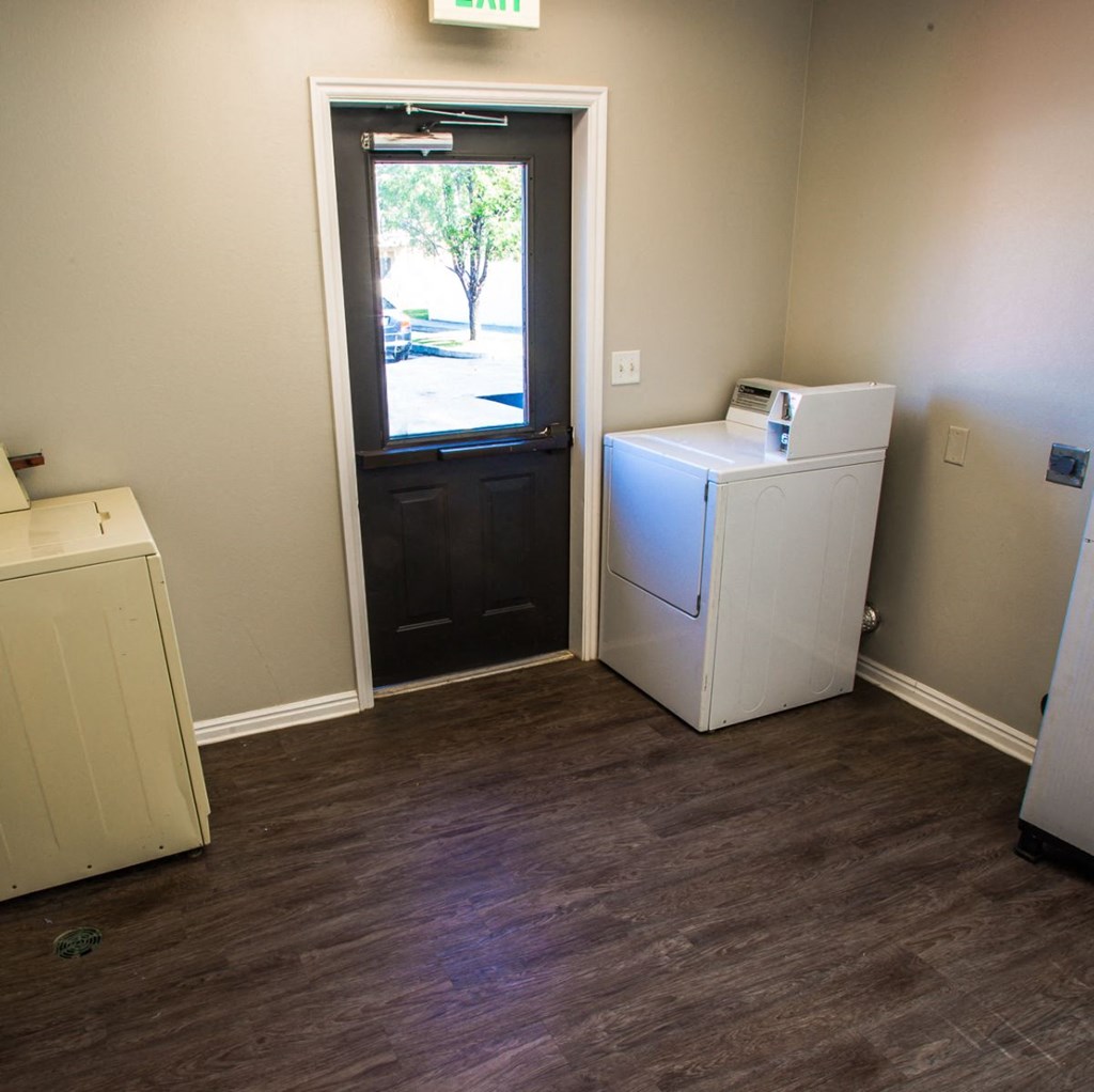A white dryer is sitting next to a white washer in a room with a door leading outside.