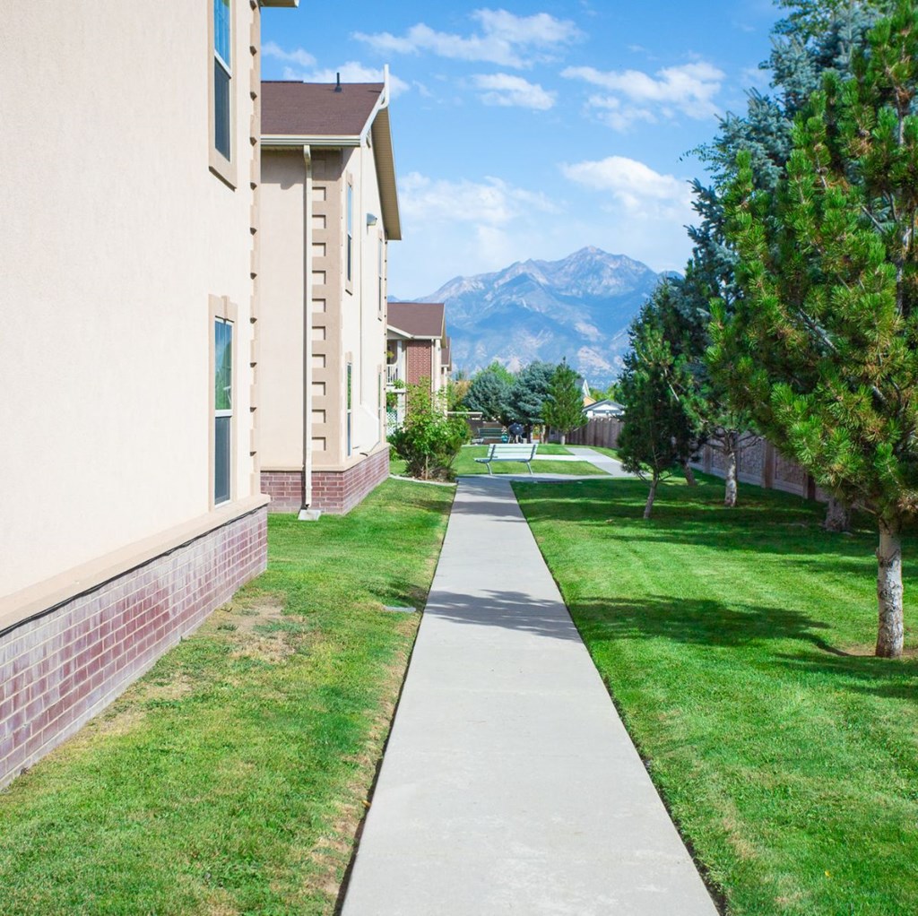 A long concrete walkway leads through a grassy area in front of a building.
