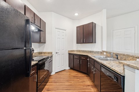A kitchen with a black refrigerator and brown cabinets.