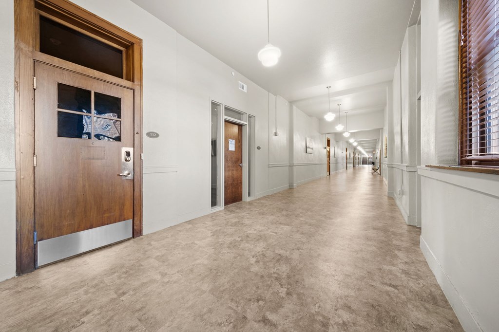 a long hallway with doors and white walls and a concrete floor