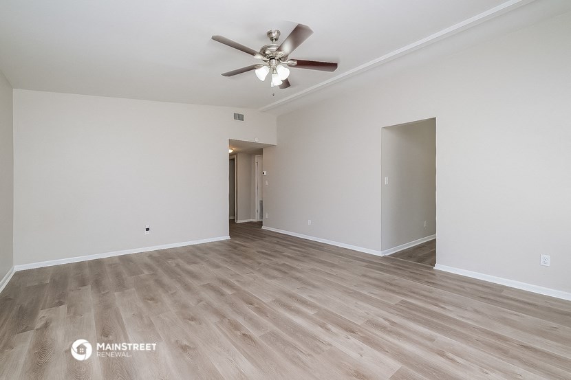 a spacious living room with white walls and a ceiling fan