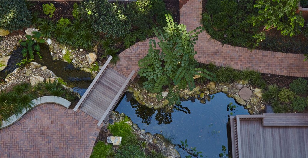 an aerial view of a garden with a pond and a bridge