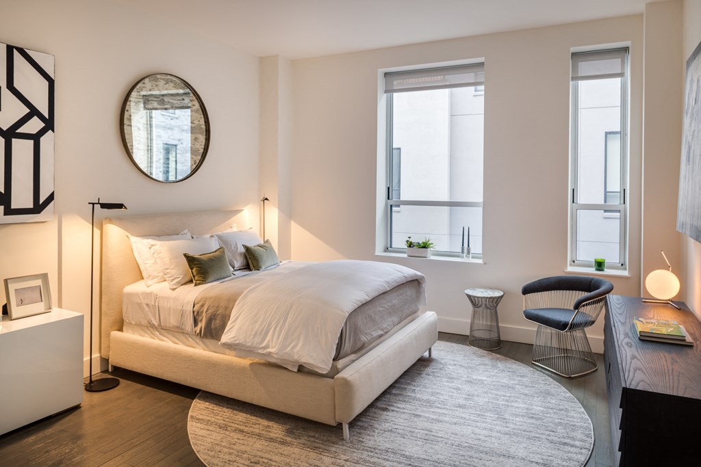 a bedroom with a bed and a round rug and two windows