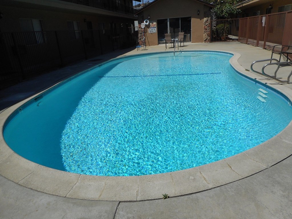 a large swimming pool in front of a building with chairs and a blue pool water